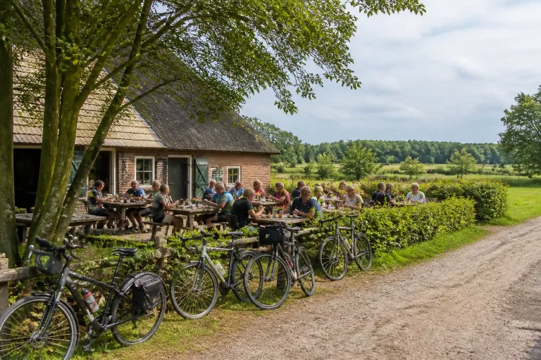 fietsers nemen eetpauze op rustig boerderijterras met geparkeerde fietsen en groen drents landschap eromheen